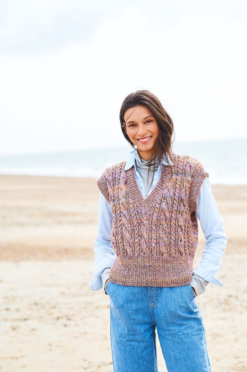 A woman is wearing a knitted tank top in shades of brown, purple and yellow.
