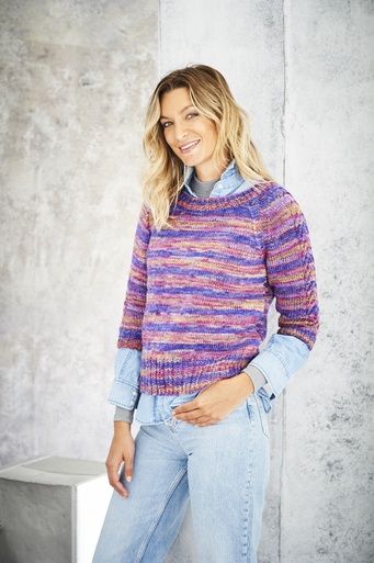 A woman is wearing a knitted sweater in a variegated purple yarn.