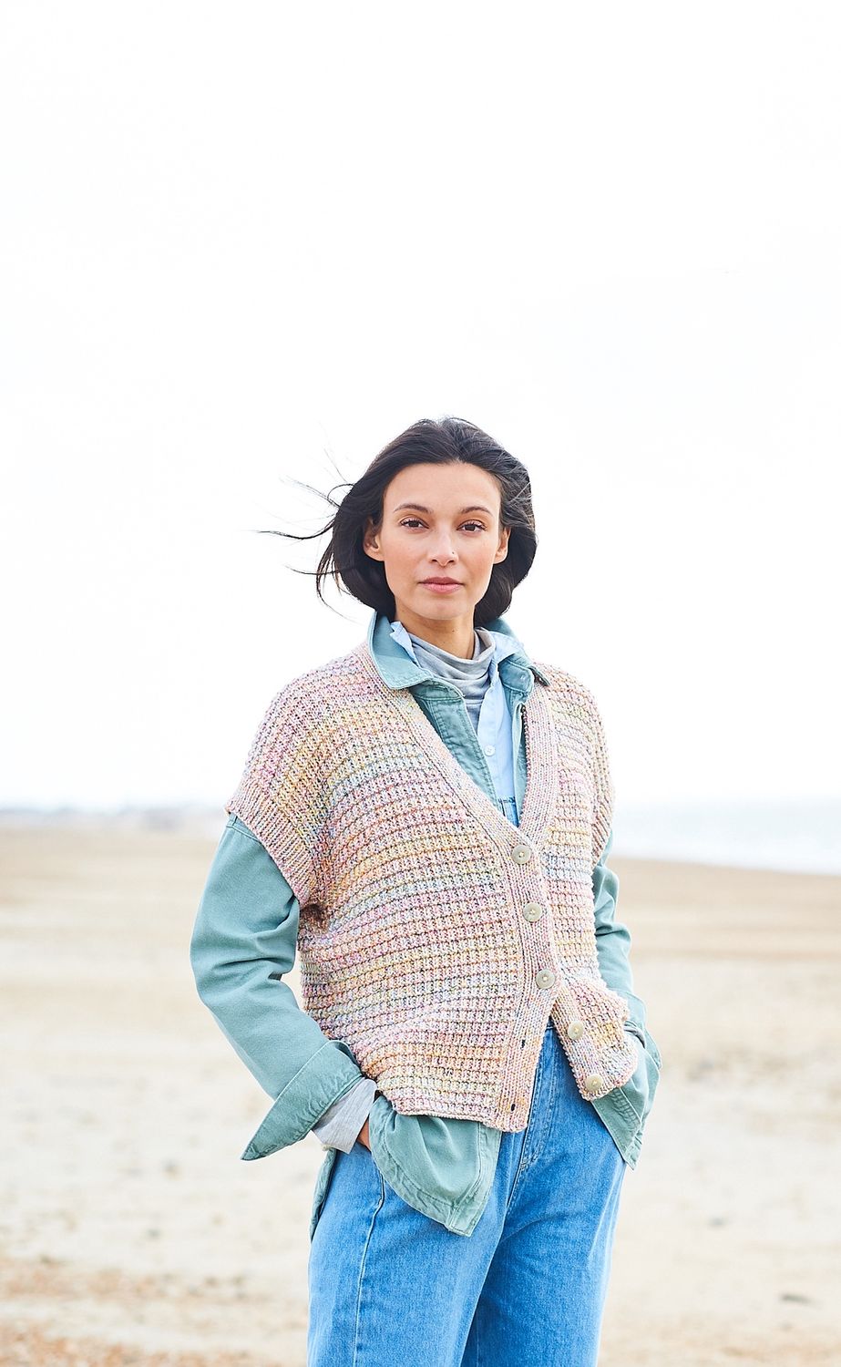 A woman is wearing a knitted waistcoat in shades of pink, blue, green and yellow.