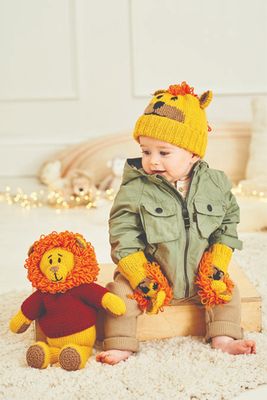 A baby is wearing a yellow knitted lion hat and matching mittens, while sitting next to a knitted toy lion in a red sweater.