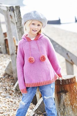 A girl is wearing a pink knitted hoodie with red hood, cuffs and pompoms.