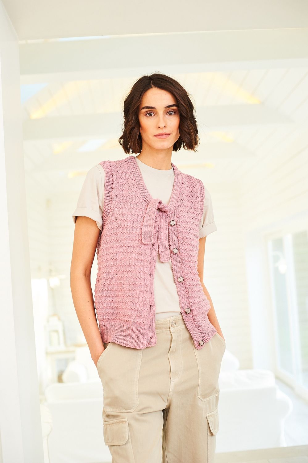 A woman is wearing a knitted waistcoat in mid pink.