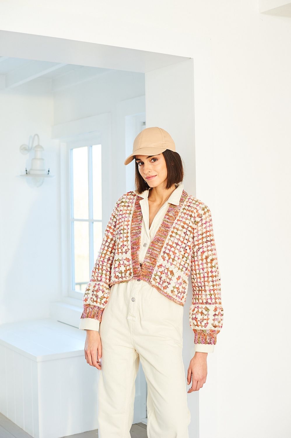 A woman is wearing a crocheted cardigan in shades of pink and cream.