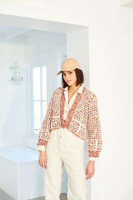 A woman is wearing a crocheted cardigan in shades of pink and cream.