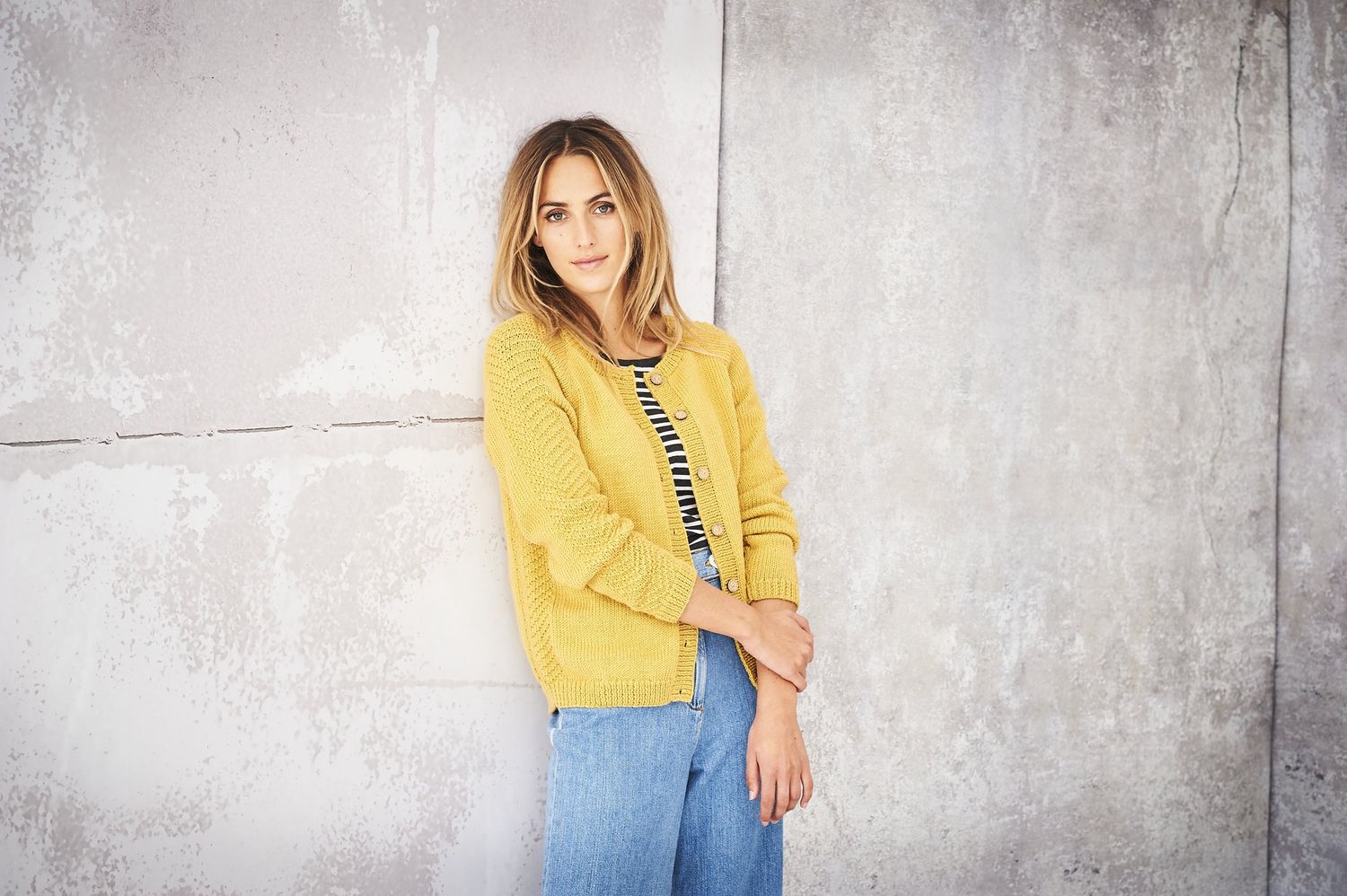 A woman is wearing a yellow knitted cardigan with textured sleeves.