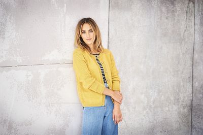 A woman is wearing a yellow knitted cardigan with textured sleeves.