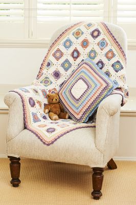 A crocheted blanket made up of cream, peach, blue, blue and green squares, alongside a matching cushion.