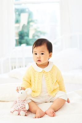 A baby is wearing a yellow cardigan with lace detail on the front.