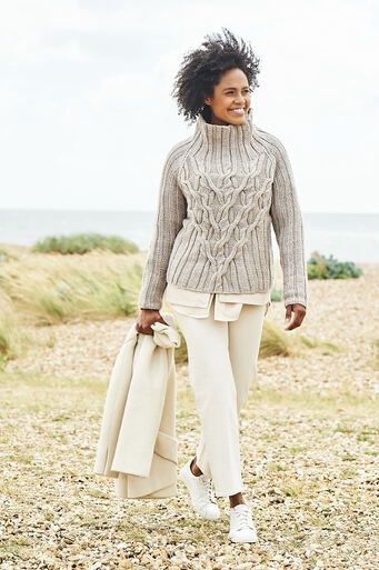 A woman is wearing a beige cable knit sweater.