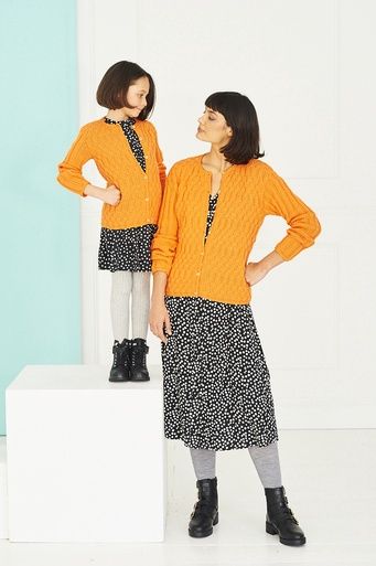 A woman and a girl are wearing matching orange knitted cardigans.