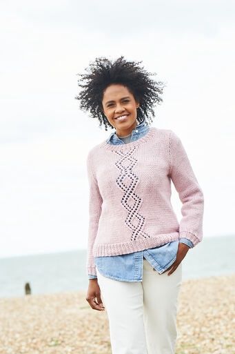 A woman is wearing a pink knitted sweater with diamond lace detail on the front.