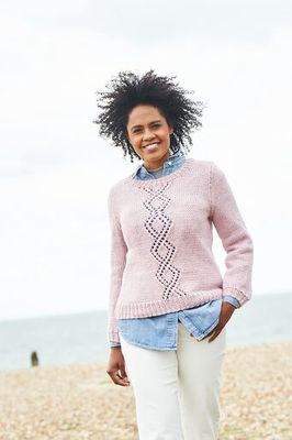 A woman is wearing a pink knitted sweater with diamond lace detail on the front.