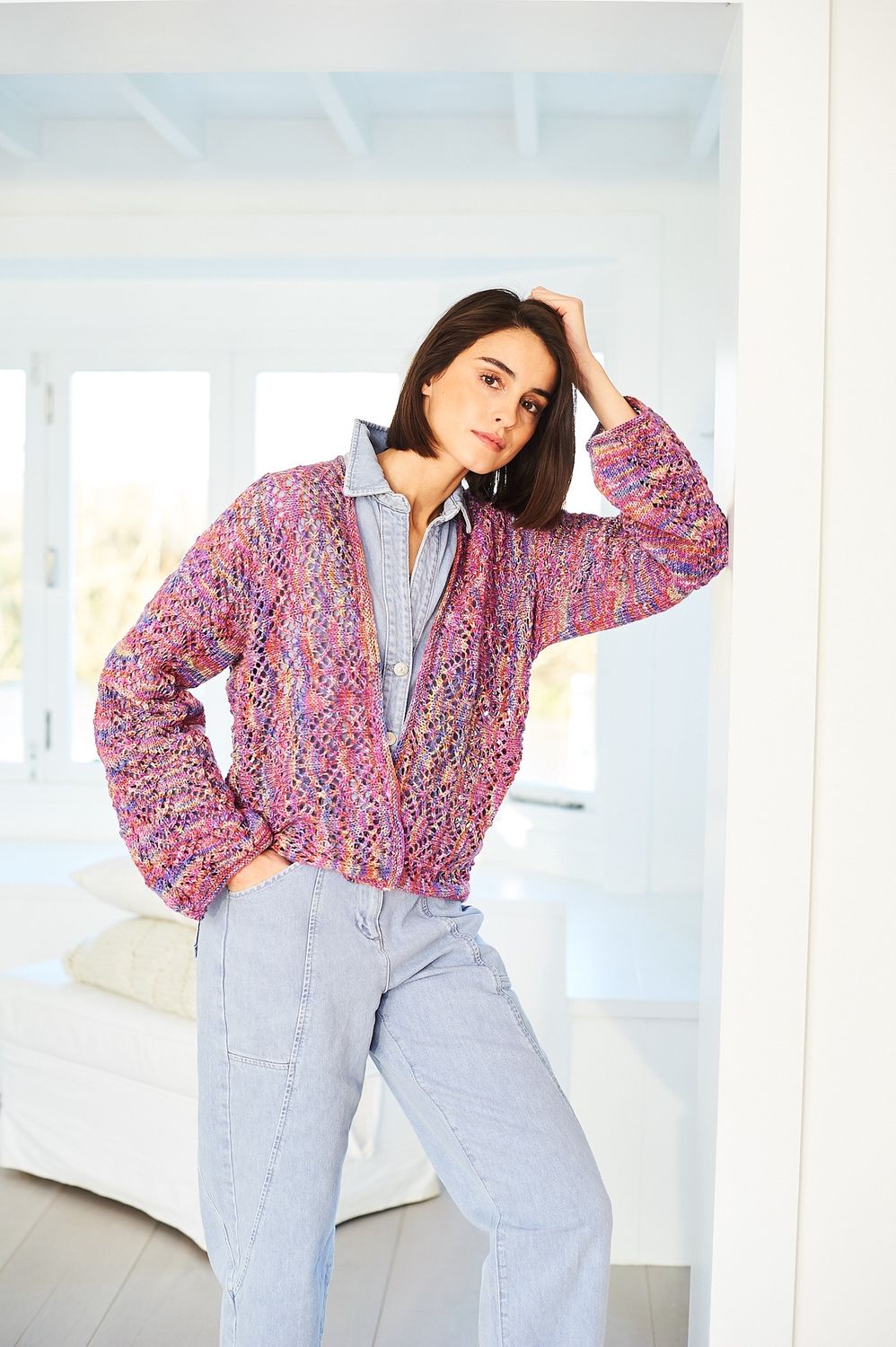 A woman is wearing a knitted jacket in a variegated pink and purple yarn.