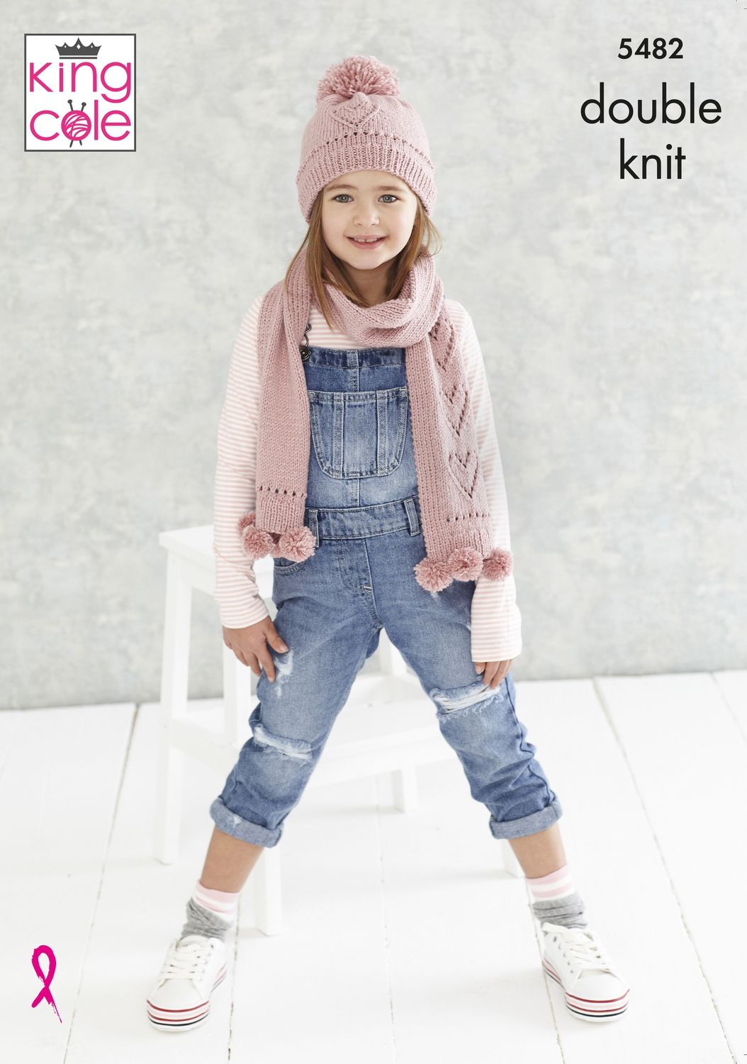 A girl is wearing a pink knitted hat and scarf with lace heart detail and pompoms.