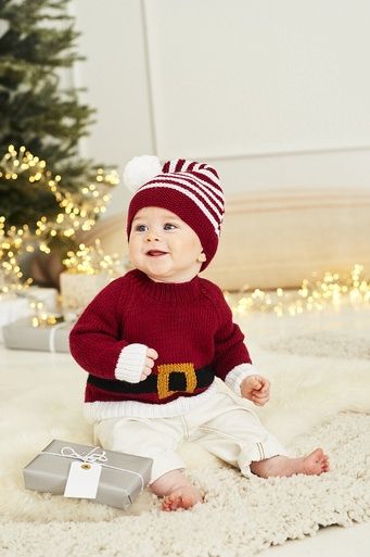 A baby is wearing a red knitted sweater to look like Santa&#39;s sweater and a red and white stripy knitted hat.