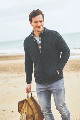 A man is wearing a black knitted cardigan with cable down the sleeves.