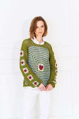 A woman is wearing a green crocheted sweater with granny squares on the front, back and sleeves.
