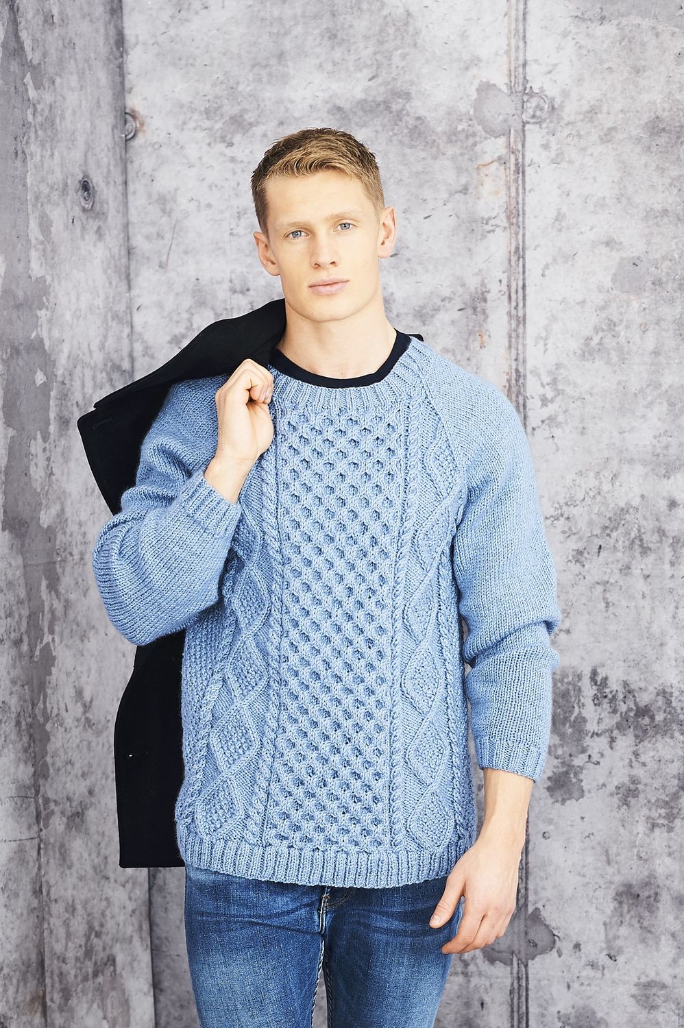 A man is wearing a blue cable knit sweater.