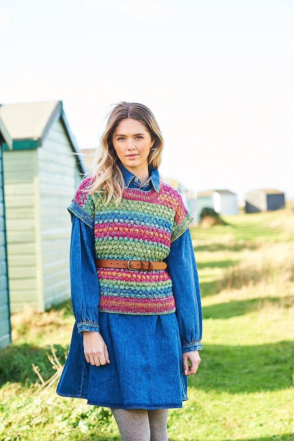 A woman is wearing a knitted top in shades of green, red and blue.