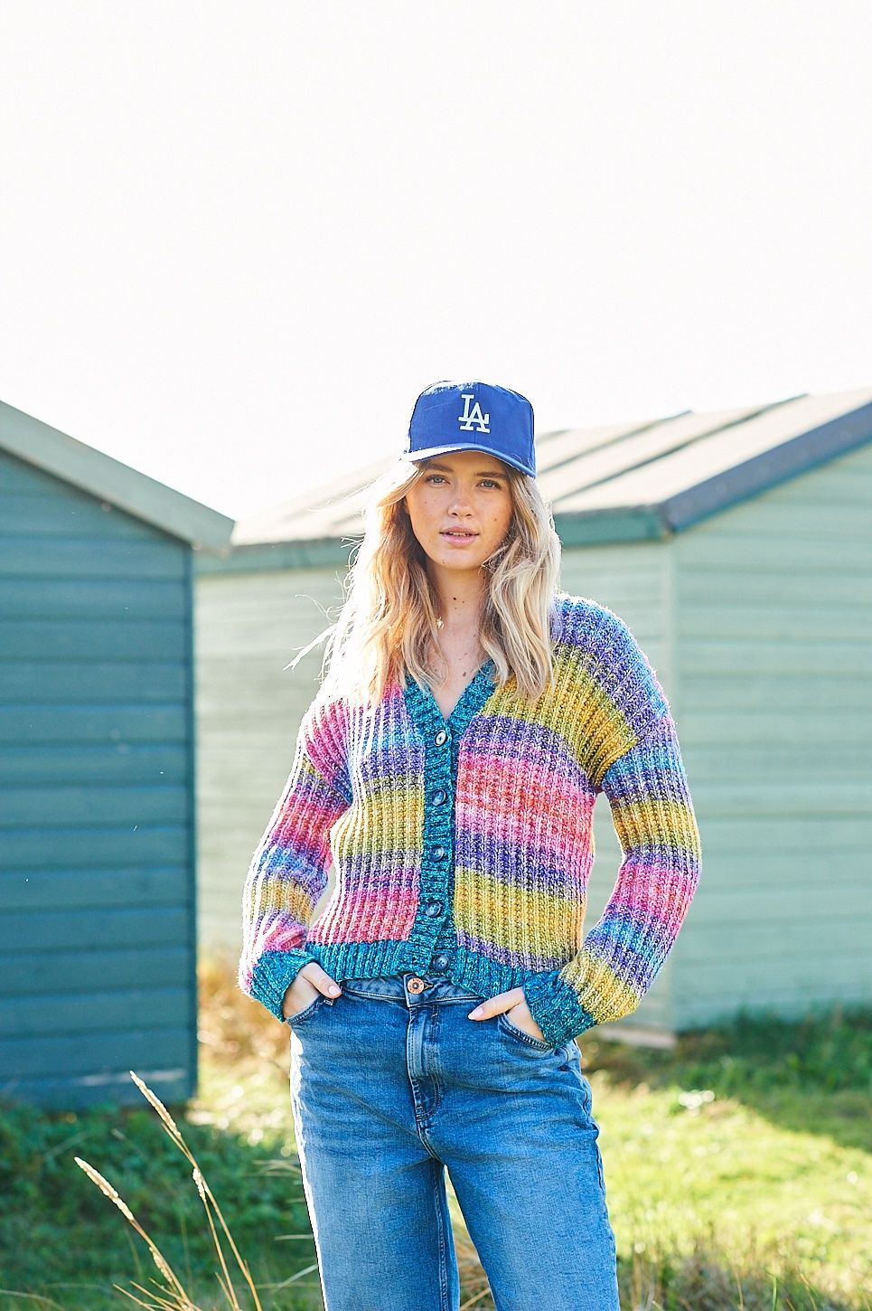 A woman is wearing a knitted cardigan in shades of red, purple, blue and green.