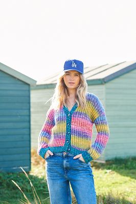 A woman is wearing a knitted cardigan in shades of red, purple, blue and green.