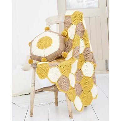 A crocheted blanket made up of yellow, cream and light brown hexagons, along with a matching cushion.