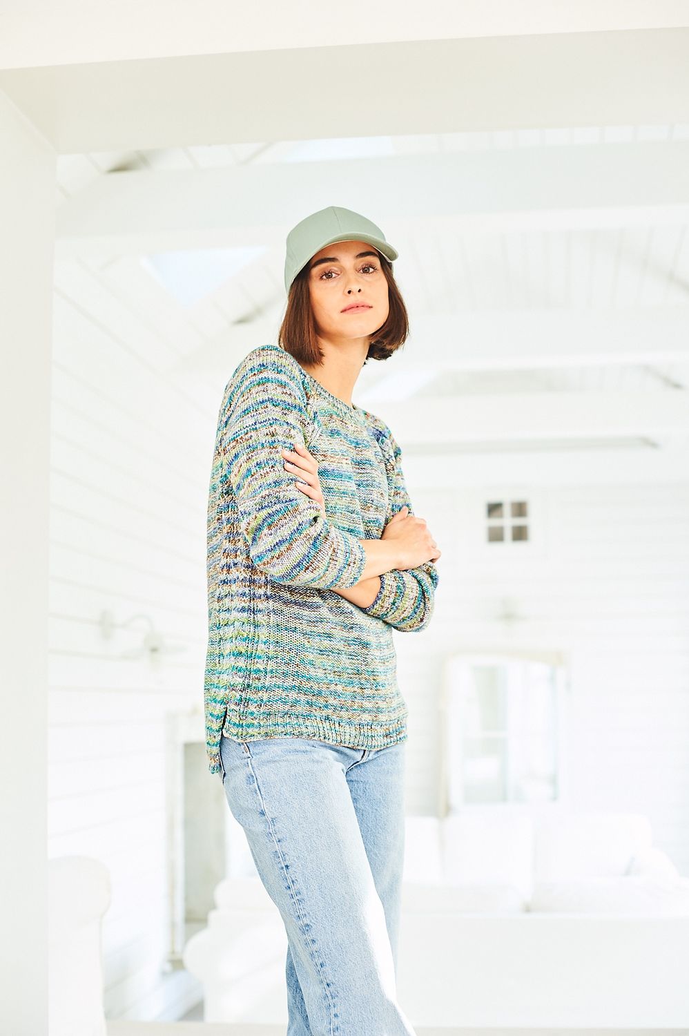 A woman is wearing a knitted sweater in a variegated blue, green and brown yarn.