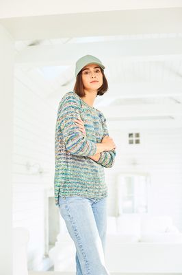 A woman is wearing a knitted sweater in a variegated blue, green and brown yarn.