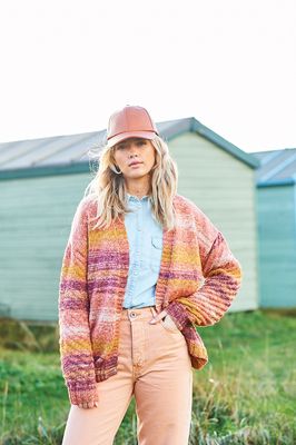 A woman is wearing a knitted cardigan in shades of pink, orange and yellow.