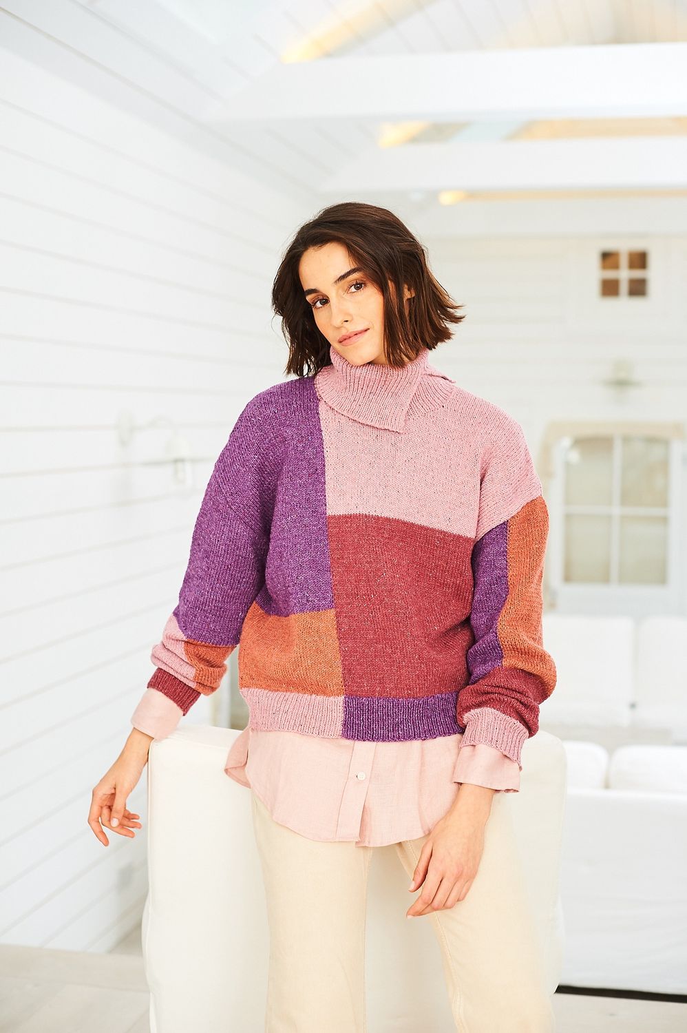 A woman is wearing a colour block knitted sweater in shades of purple, pink and orange.