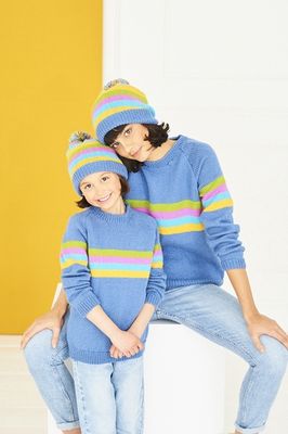 A woman and a girl are wearing matching blue knitted sweaters and hats with green, pink, aqua and yellow stripes.