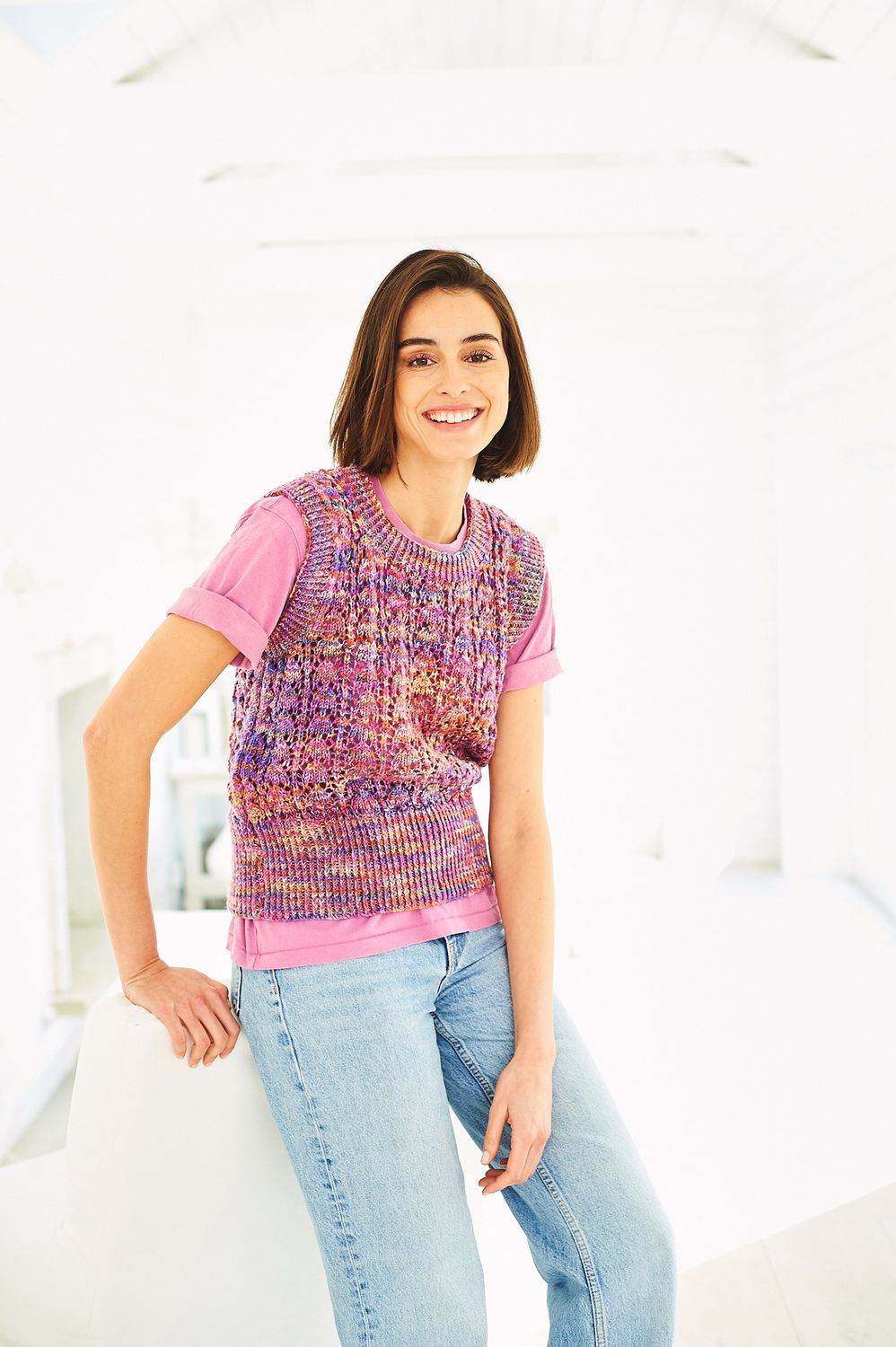 A woman is wearing a knitted tank top in a variegated pink, purple and yellow yarn.