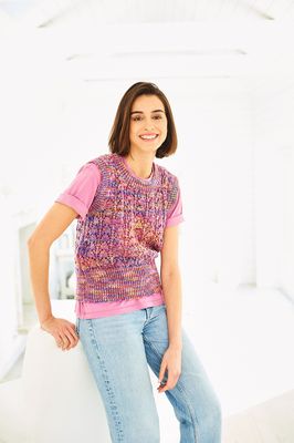 A woman is wearing a knitted tank top in a variegated pink, purple and yellow yarn.