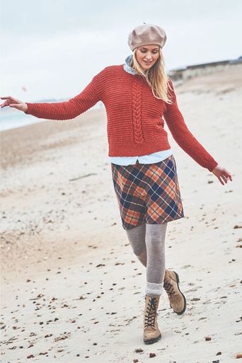 A woman is wearing a red knitted sweater with a cable panel down the centre.