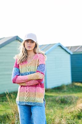 A woman is wearing a knitted sweater in shades of red, coral, yellow, green and blue.