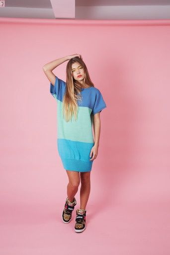 A woman is wearing a knitted dress in blocks of dark blue, mint green and bright blue.