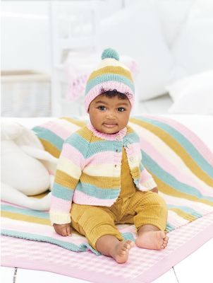 A baby is wearing a striped cream, pink, blue and yellow knitted cardigan with a matching hat and blanket.