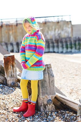 A girl is wearing a variegated knitted hoodie in shades of blue, orange, pink, yellow, green and purple.