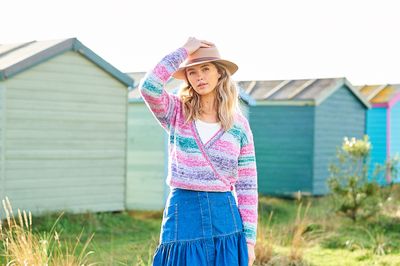 A woman is wearing a knitted wrap cardigan in shades of pink, purple and teal.