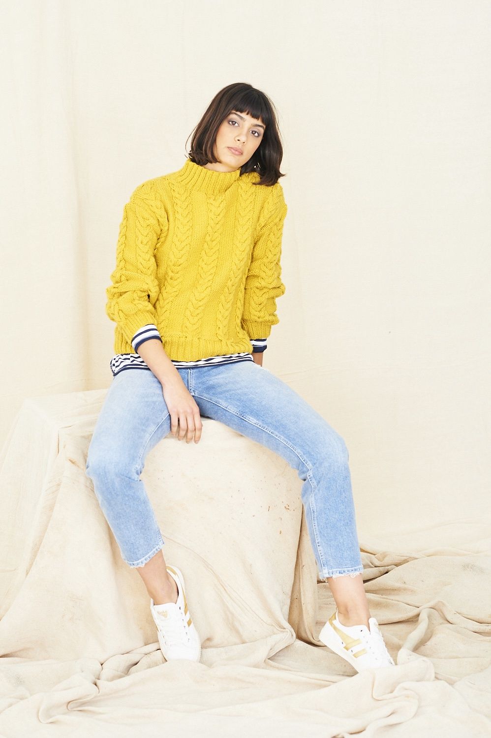 A woman is wearing a yellow cable knit sweater.