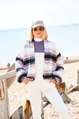 A woman is wearing a variegated cropped knitted cardigan in shades of cream, grey and pink.