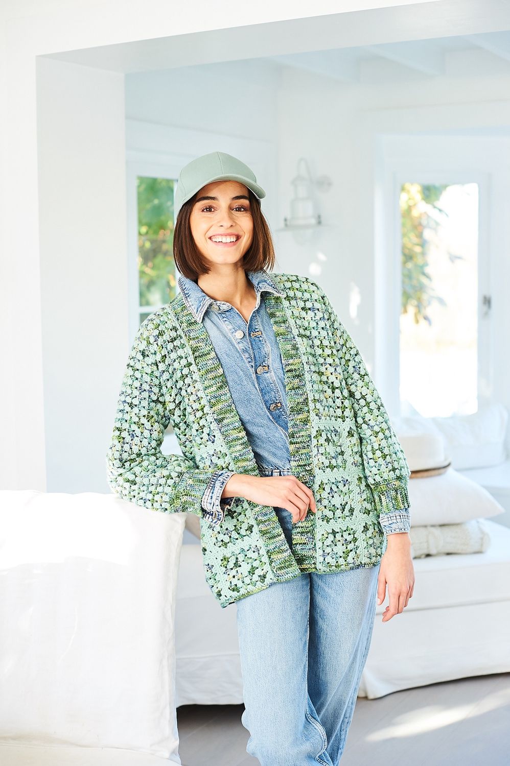 A woman is wearing a crocheted cardigan in shades of green.
