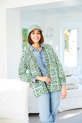 A woman is wearing a crocheted cardigan in shades of green.
