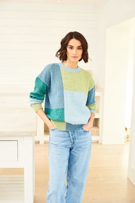 A woman is wearing a colour block knitted sweater in shades of blue and green.