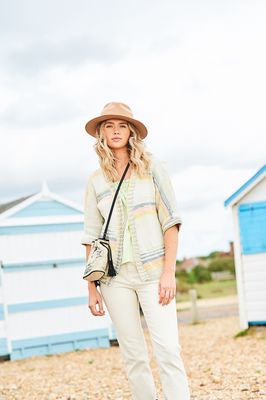 A woman is wearing a short knitted cardigan in shades of cream, grey, yellow, peach and green.