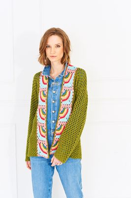 A woman is wearing a green crocheted cardigan with rainbow granny squares on the front and back.