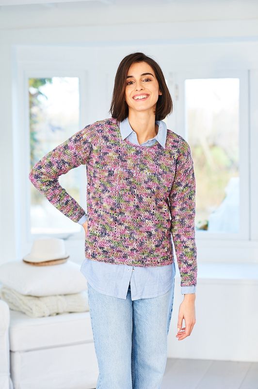 A woman is wearing a crocheted sweater in a variegated pink, purple and green yarn.