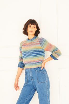 A woman is wearing a knitted sweater in shades of blue, red, orange, yellow, green and purple.