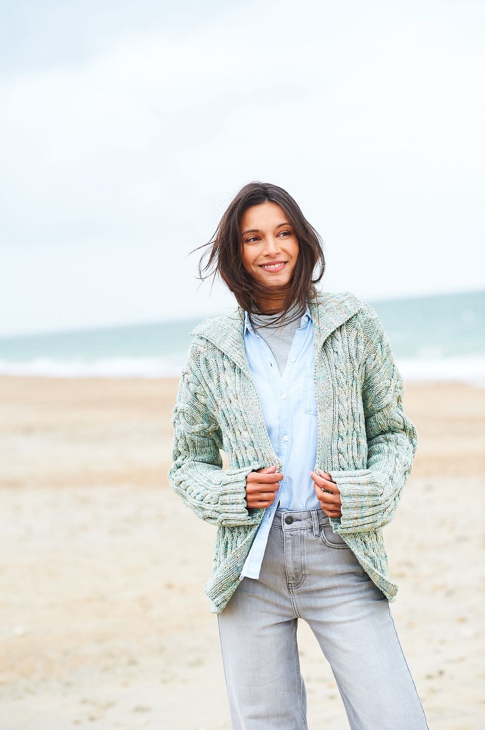 A woman is wearing a knitted jacket in shades of green.