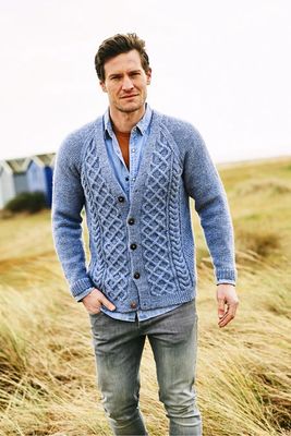 A man is wearing a light blue cardigan with a cable design on the front.